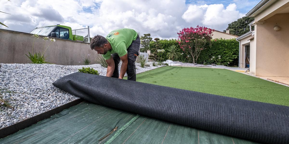 Vue large d'un terrain de jardin résidentiel préparé montrant les différentes couches de fondation en gravier et sable compacté, chantier propre sans présence humaine, maison contemporaine française en arrière-plan